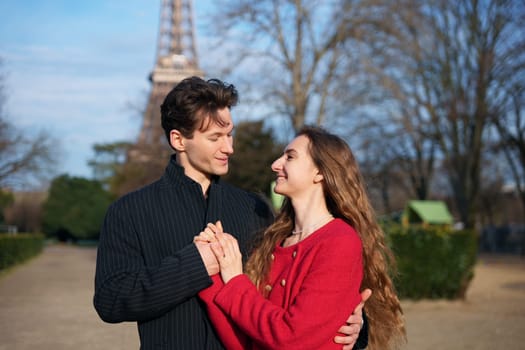 A happy couple shares a warm embrace near the Eiffel Tower in Paris. They smile affectionately, enjoying a romantic moment together.