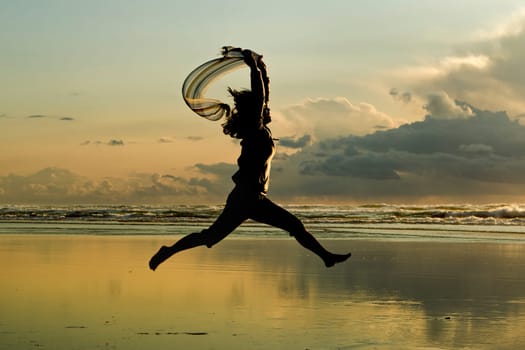 A woman with a scarf leaps on the beach in Newport, Oregon.