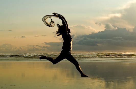 A woman with a scarf leaps on the beach in Newport, Oregon.