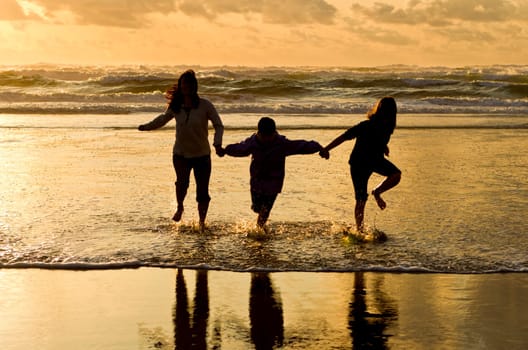 A mother, daughter, and son, walk in the water at the beach in Newport, Oregon.