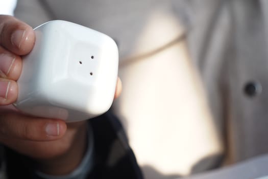 A person is holding a square salt shaker while seated at a table.