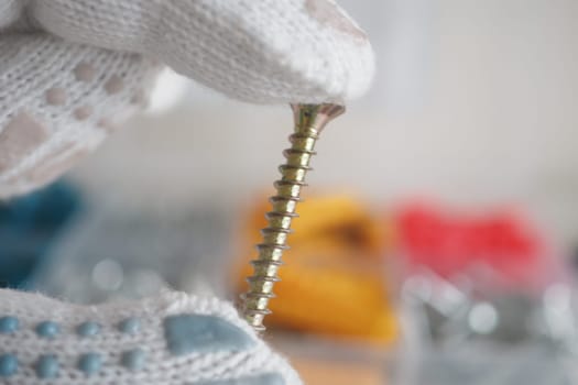 Close-up of a hand holding a screw with tools in the background.