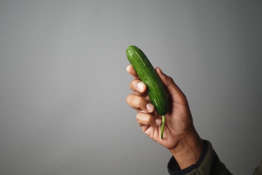 A hand is holding a vibrant green cucumber, ready for use in cooking.