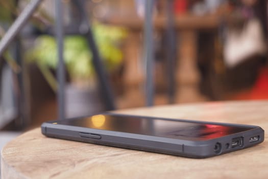 A smartphone is placed on a wooden table next to lush plants inside a cafe.