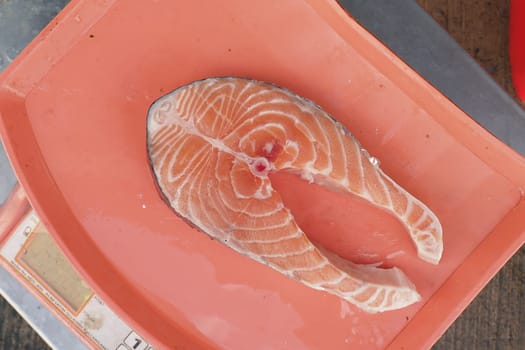 A salmon fillet is carefully placed on a scale at a market.