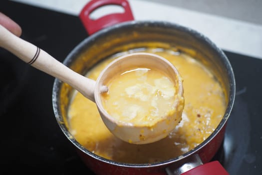 A wooden ladle scoops soup from a red pot on the stovetop.