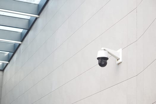 A security camera is installed on a smooth wall below a glass ceiling.