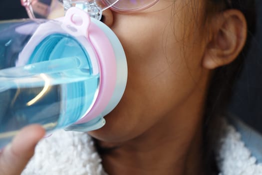 A child sips water from a cheerful, colorful drinking bottle.