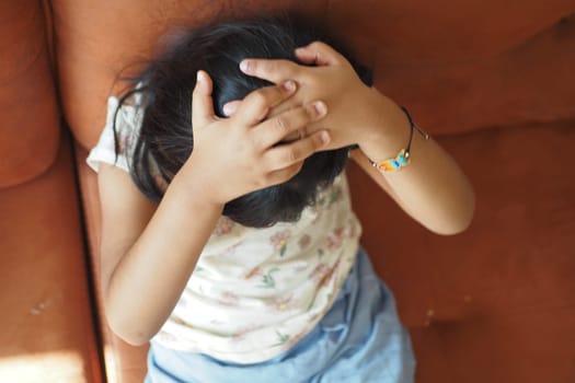 A child sits on a couch, holding their head with both hands, expressing stress.