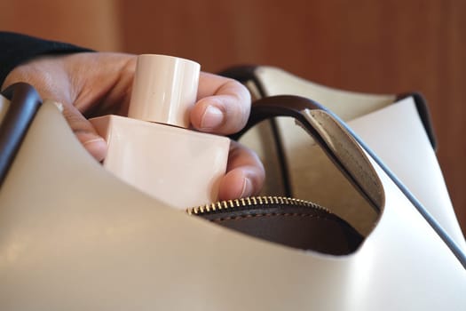 A hand is gently inserting a perfume bottle into a handbag.