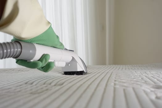 A person uses a steam cleaner to sanitize a mattress surface.