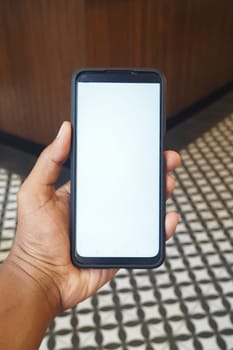 A person is holding a blank smartphone in a trendy cafe with patterned tiles.