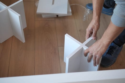 Individual is working on furniture assembly using white components.