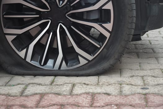 A stylish car has a flat tire while parked on a cobblestone street.