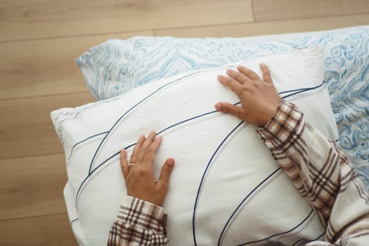 A person relaxes with hands on a soft pillow in a cozy bedroom.