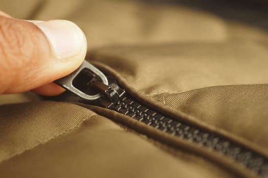 Close-up of a hand gripping a zipper on a brown jacket during daytime.