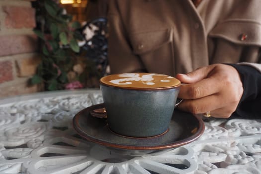 A person enjoys a beautifully crafted coffee at a cafe table.
