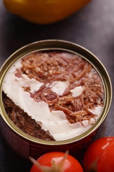 Canned meat sits open on a kitchen counter beside fresh tomatoes.