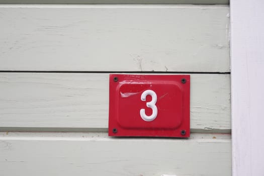 A bright red number three is mounted on a light green wooden wall.