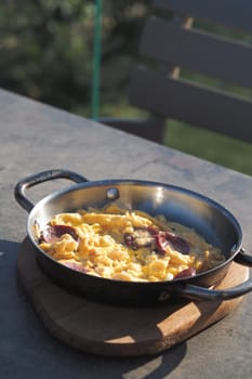 A warm skillet holds fluffy scrambled eggs with sausage, outside.