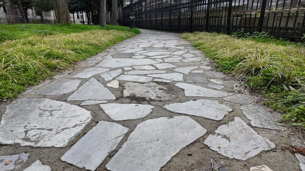 A well-worn stone pathway leads through a peaceful park, bordered by grass.