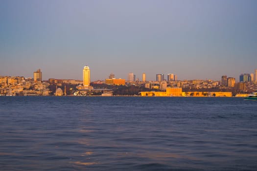 The city skyline shimmers in golden light as the sun sets over water.