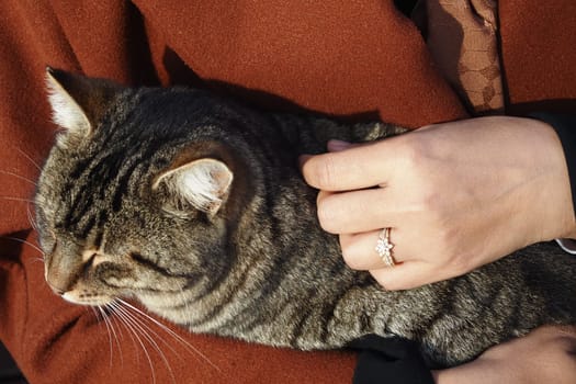 A woman in a warm outfit holds a striped cat lovingly while relaxing.