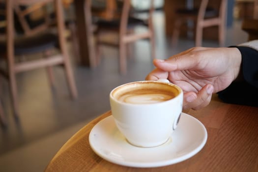 A hand holds a steaming cup of coffee while relaxing in a cafe.