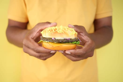 A person displays a vibrant burger with unique ingredients and toppings.