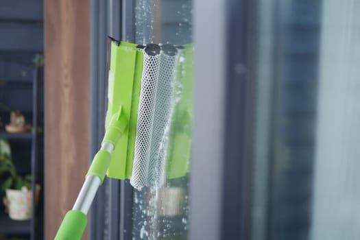 A person is cleaning a glass window using a squeegee tool indoors.