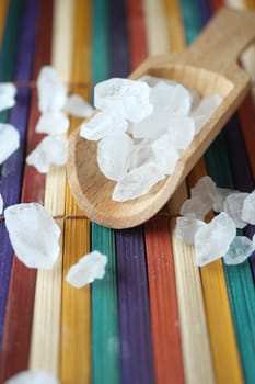 Sea salt crystals are arranged on a vibrant wooden surface with a scoop.