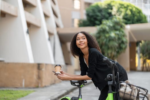 Focused on her sustainable living goals, this woman enjoys a coffee break, leaning on her vibrant green bicycle amidst an urban backdrop, connecting with her city.