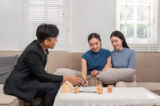 In a bright and inviting living room, a real estate agent engages with two clients, highlighting various property choices and answering their questions, fostering a collaborative atmosphere.