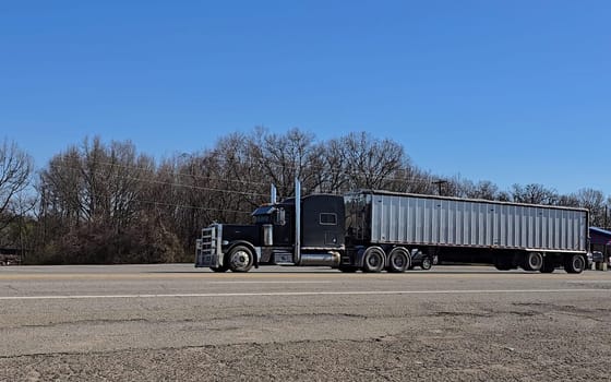 Freight liner Semi-Truck Driving on Open Highway in a Rural Area, CDL Truck America, semi truck and trailer travels along an open road under a blue sky in a rustic rural setting, showcasing commercial transportation, logistics efficiency, and professional trucking