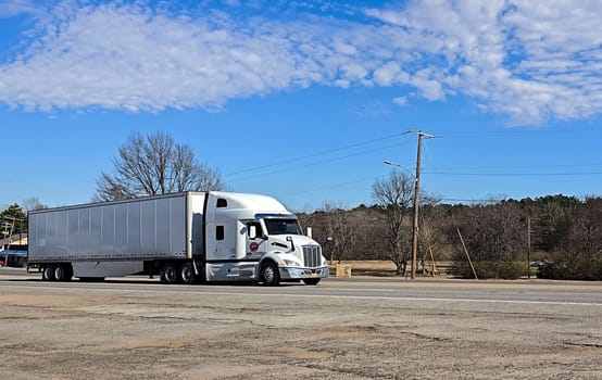 Freight liner Semi-Truck Driving on Open Highway in a Rural Area, CDL Truck America, semi truck and trailer travels along an open road under a blue sky in a rustic rural setting, showcasing commercial transportation, logistics efficiency, and professional trucking