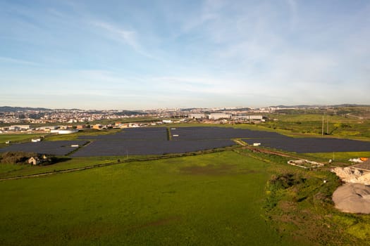 Aerial shot of solar panels in field, vast landscape with green energy and townscape in distance under clear sky during daytime