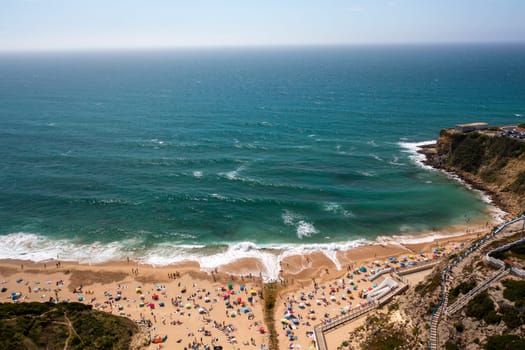 Aerial drone view of tourists on sandy seashore at Magoito Beach. Sea waves splash on the coast of a famous destination in Sintra, Portugal, during summer