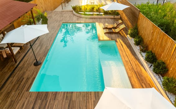 Elegant backyard with turquoise swimming pool, wooden deck, umbrellas, and lounge chairs in a sunny setting