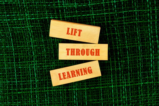Wooden blocks with the words lift through learning placed on a textured green surface, symbolizing the importance of education and growth
