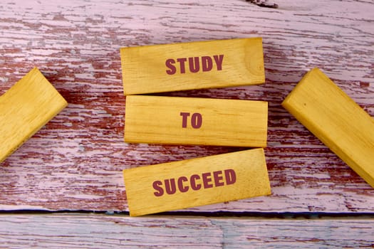 Wooden blocks displaying the words study to succeed are arranged on a rustic pink surface promoting the value of education and learning