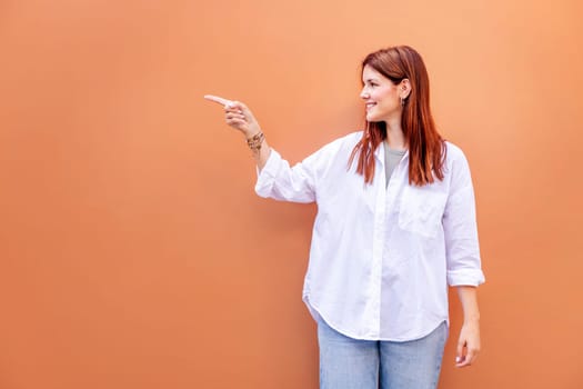 smiling young woman in white shirt and blue jeans is pointing to the side, copyspace for text