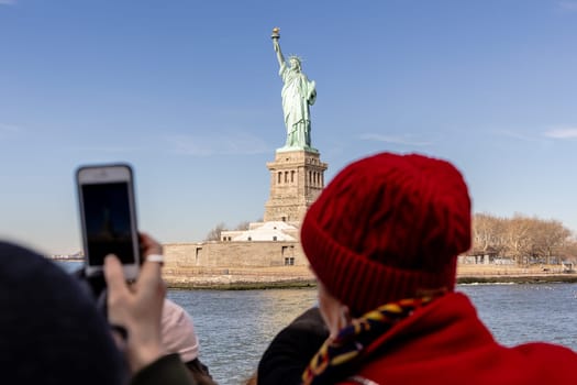 New York City, USA - February 13, 2023 - Tourists taking photos of the Statue of Liberty aboard a ferry from Manhattan to Liberty Island on a winter day