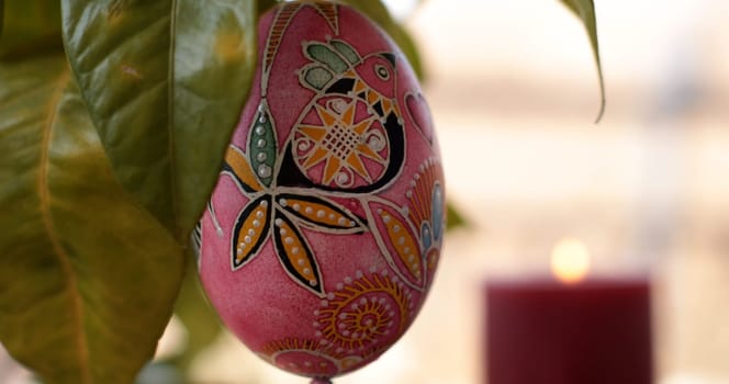 Handcrafted Easter egg dot art pysanka showcases vibrant colors and designs, hanging amongst lush greenery. This decoration invites a festive atmosphere, complementing any Easter celebration.