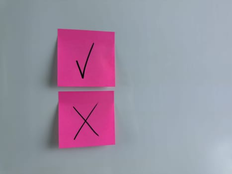 Making management decision in company and marking important choice with special symbols. Sticky note on white background with check mark and cross to indicate choice and decision