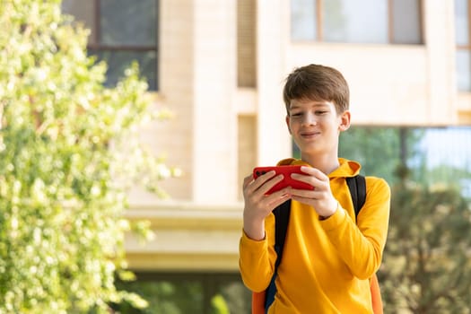 A teenage boy stands in front of a high-rise apartment building, holding a smartphone and smiling while looking at the screen. Represents modern digital life, communication, and urban lifestyle.