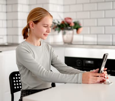 Cute Little Girl Talking Via Video Call Online Using A Smartphone In The Kitchen