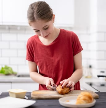 Pretty Young Girl Cuts A Croissant For Breakfast