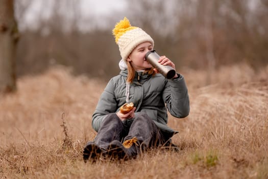 Girl Drinks Tea From A Thermos And Eats A Croissant In Nature In Spring