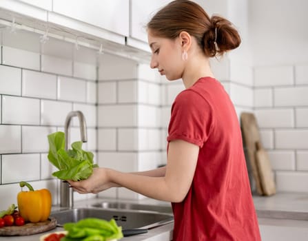 Young Girl Washes Lettuce Leaves In The Kitchen At Home