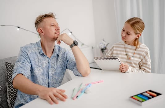 Little Girl Drawing A Portrait Of Dad, Happy Family At Home Having Fun